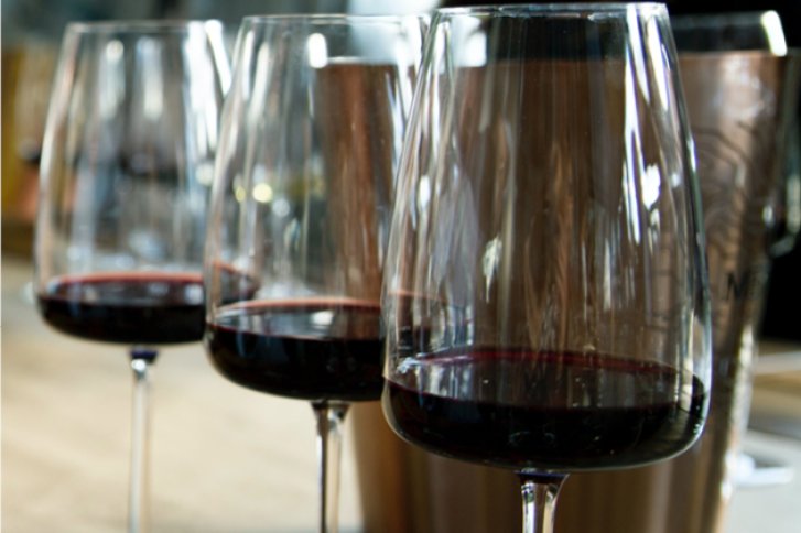 Drei Rotweingläser stehen nebeneinander auf einem Tisch in einem gemütlichen Raum.