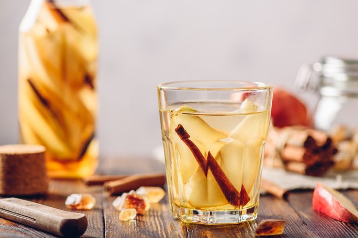 Glas enthält Getränk mit Birnenstücken und Zimtstange, umgeben von Dekorationen auf holzfarbenem Tisch.