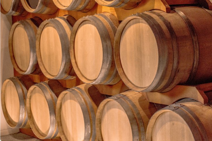 Holzfässer stehen gestapelt in einem Lagerraum zur Reifung von alkoholischen Getränken.