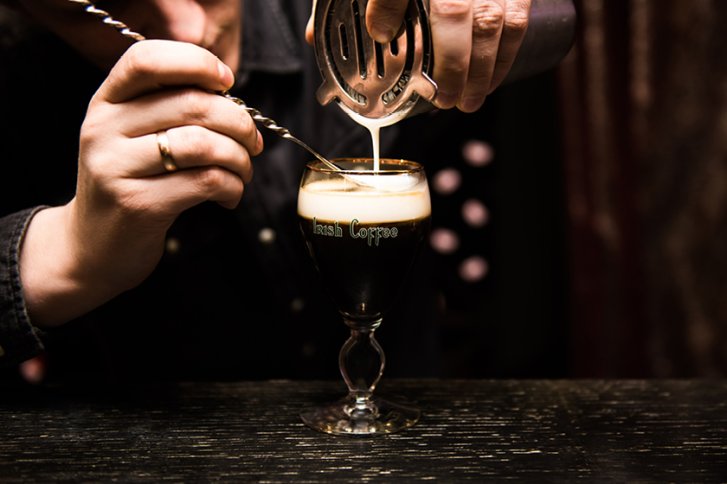 Ein Glas Irish Coffee wird sorgfältig von Hand mit Sahne befüllt.