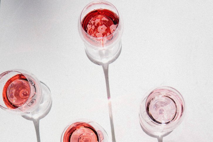 Vier Weingläser mit rosafarbenem Wein stehen auf weißem Hintergrund, von oben betrachtet.