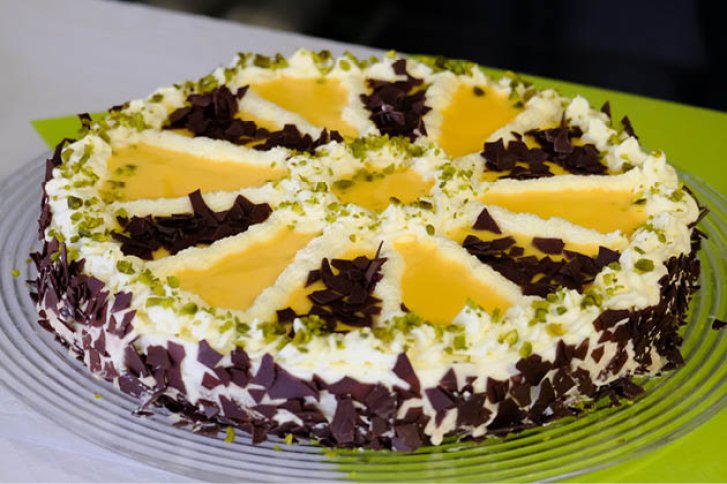 Kuchen mit Sahne, Mangosoße und Schokoraspeln, dekoriert auf Glasscheibe vor grünem Hintergrund.