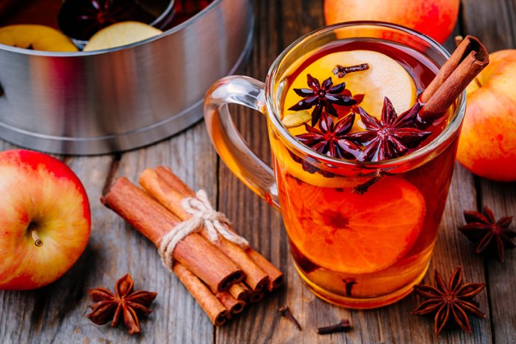 Glas mit heißen Apfelwein, Zimt und Sternanis, auf einem Holztisch mit Äpfeln.