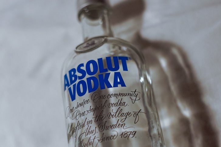Vodkaflasche liegt auf weißem Untergrund, blauer Text "Absolut Vodka", elegant geschwungene Schrift darunter.