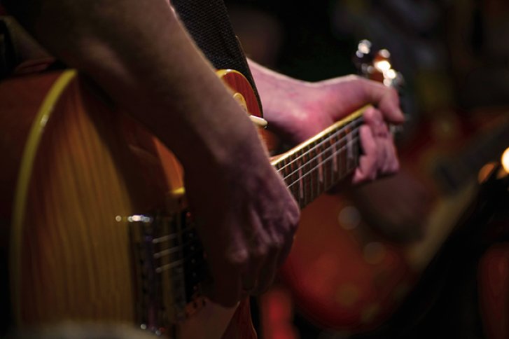 Musiker spielt E-Gitarre auf einer Bühne in gedämpftem Licht.