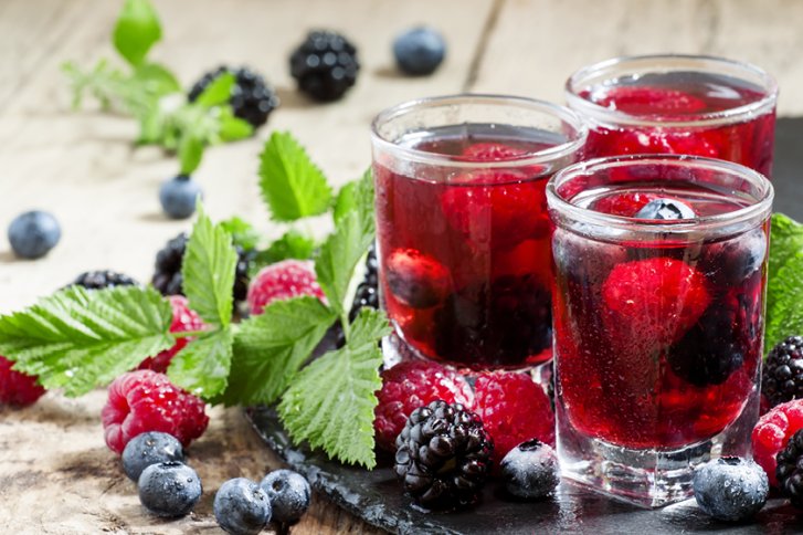Gläser mit rotem Getränk stehen auf dem Tisch, umgeben von Beeren und Blättern.