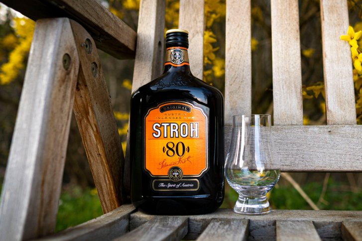 Eine Stroh 80 Flasche steht neben einem Glas auf einem Holztisch im Freien.