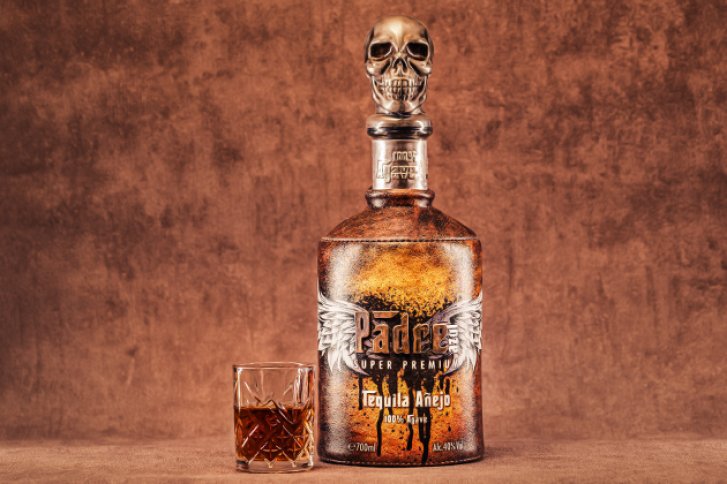 Flasche mit Totenkopfdeckel steht neben Glas, auf rustikalem Hintergrund, Text: "Padre Tequila Añejo".