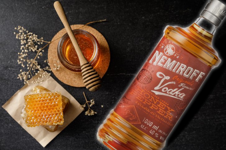 Flasche Nemiroff Vodka liegt auf Tisch neben Honigglas, Honigwabe und getrockneten Blumen.