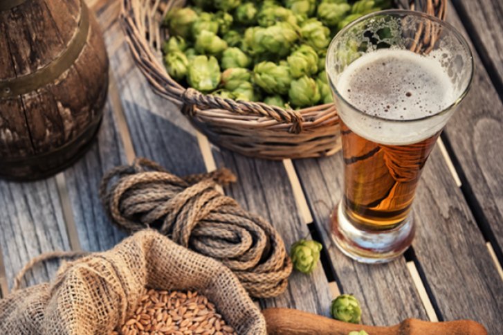 Ein Bierglas steht auf Holztisch, umgeben von Hopfen, Getreide und einem Seil.