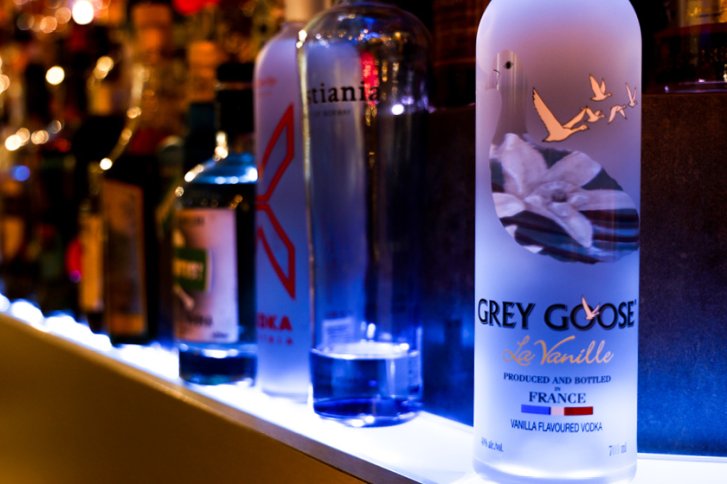 Flaschen stehen nebeneinander auf beleuchtetem Regal; Fokus auf Grey Goose La Vanille Vodka.