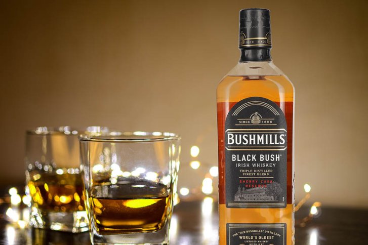 Whiskeyflasche steht neben zwei gefüllten Gläsern auf Tisch, umgeben von Lichterketten.