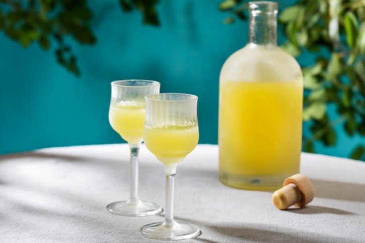 Zwei gefüllte Gläser und eine Flasche mit gelbem Getränk auf einem Tisch im Freien.