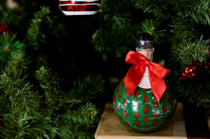 Eine dekorative Flasche mit roter Schleife steht zwischen Tannenzweigen auf einem Geschenk.