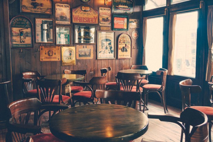 Holztische stehen in einem gemütlichen Pub, umgeben von holzgetäfelten Wänden mit Retro-Postern.