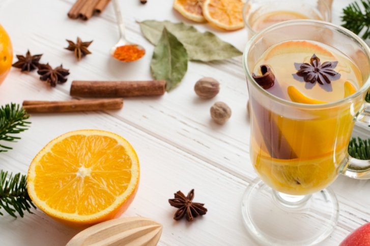 Glas Glühwein mit Orangen, Zimt und Anis auf weißem Holztisch mit Gewürzen.