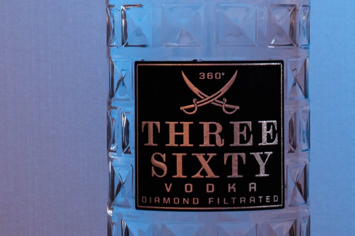 Eine durchsichtige Flasche mit Rautenmuster zeigt das Etikett "THREE SIXTY VODKA".
