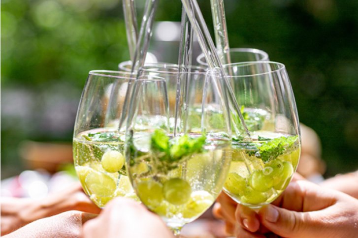 Gläser sprudelnder Getränk mit Minze und Trauben, draußen, von mehreren Händen angestoßen.