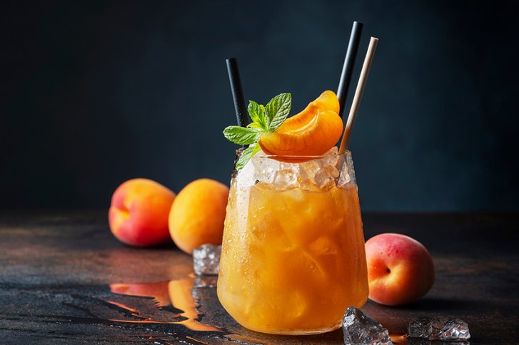 Ein Glas mit orangem Getränk und Eis, dekoriert mit Minze und Aprikosen, auf Holztisch.