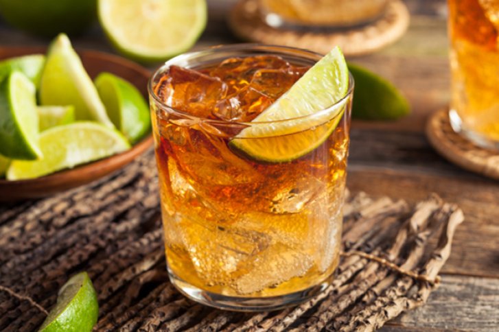 Ein Glas mit Whisky und Eis, garniert mit Limette, steht auf rustikalem Holztisch.