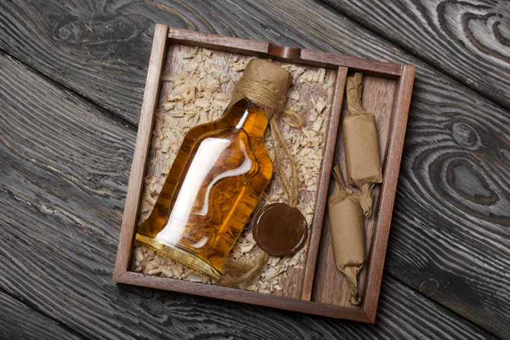 Flasche mit Schnur umwickelt, liegt auf Holzspänen in einer Holzkiste, neben eingewickelten Bonbons.