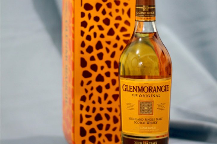 Eine Whiskyflasche steht vor einer dekorativen Schachtel mit orangefarbenem Muster auf blauem Hintergrund.