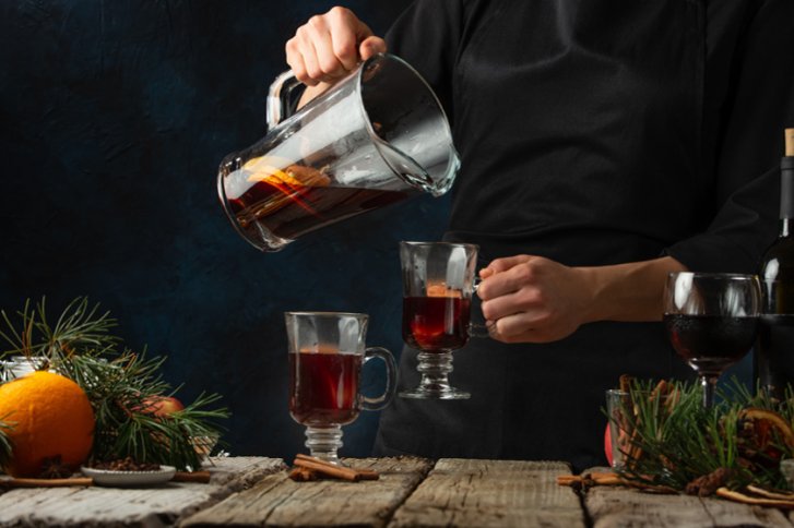 Eine Person gießt Glühwein aus einem Krug in ein Glas auf einem Holztisch.