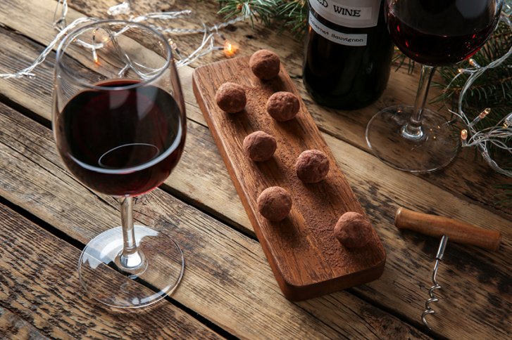 Weingläser und Trüffel liegen dekorativ auf einem Holztisch mit Lichterketten und Korkenzieher.