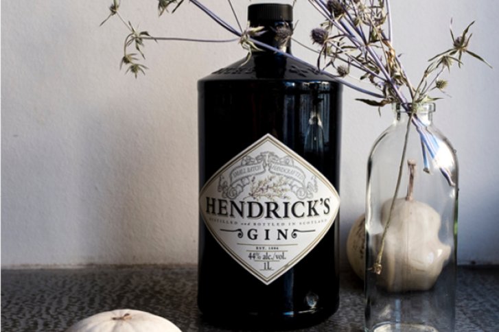 Eine schwarze Hendrick's Gin-Flasche steht neben getrockneten Blumen in einer Vase auf einem Tisch.