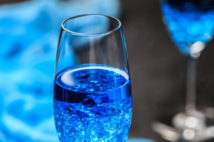 Blaues Getränk füllt ein Sektglas, im Hintergrund verschwommene blaue Töne.