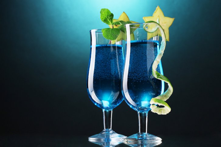 Zwei mit blauer Flüssigkeit gefüllte Gläser, mit Minze und Sternfrucht garniert, vor blauem Hintergrund.