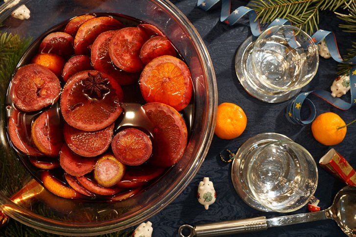 Rote Fruchtscheiben schwimmen in einer Glasschale, umgeben von Gläsern und weihnachtlicher Dekoration.