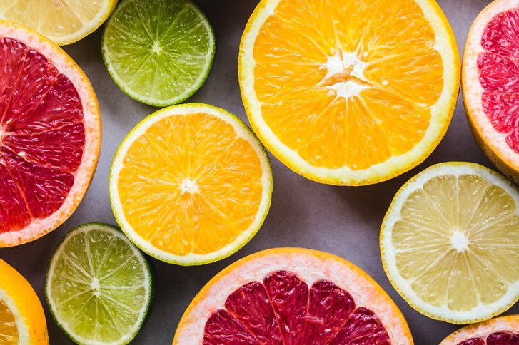 Halbierte Zitrusfrüchte liegen nebeneinander auf einem grauen Hintergrund, präsentieren bunte, frische Schnittflächen.