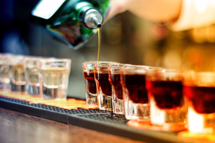 Gläser werden mit dunkler Flüssigkeit aus Flasche gefüllt, auf Tresen in Barumgebung.