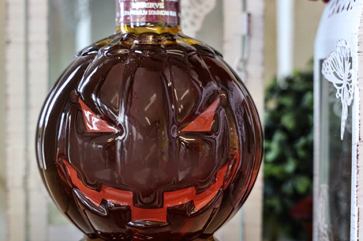 Flasche – hat ein gruseliges Kürbisgesicht – steht auf einem Regal vor unscharfer Kulisse.