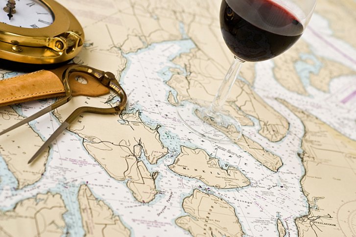 Ein Weinglas steht auf einer Seekarte neben einem Kompass und einem Navigationsinstrument.