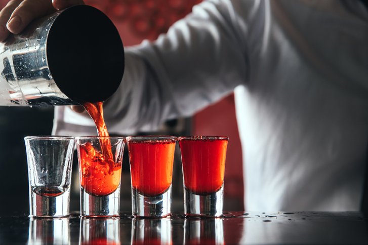 Gläser werden mit rotem Getränk aus einem Metallshaker in einer Bar gefüllt.