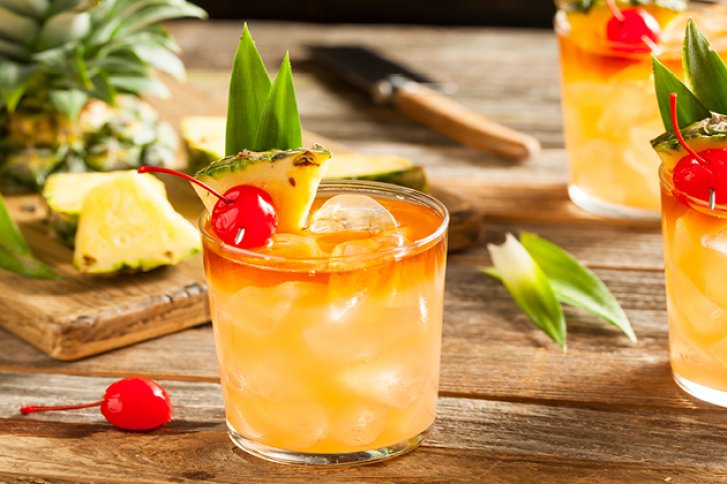 Ein Cocktail mit Ananas und Kirschen verziert steht auf einem hölzernen Tisch.