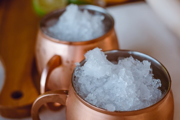 Kupferbecher gefüllt mit zerstoßenem Eis, stehend auf einem Holzbrett, Hintergrund unscharf.