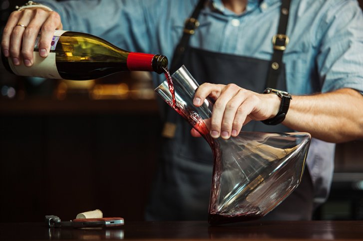 Wein wird in eine Karaffe geschenkt, von einer Person in Schürze und Hemd.