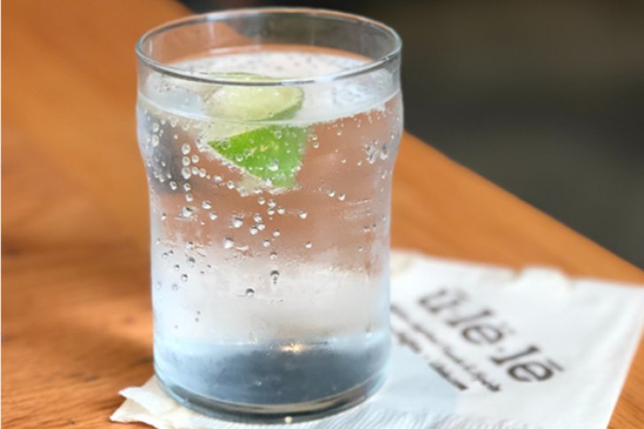 Ein Glas Wasser mit Limettenstückchen steht auf einem Holztisch neben einer Serviette.