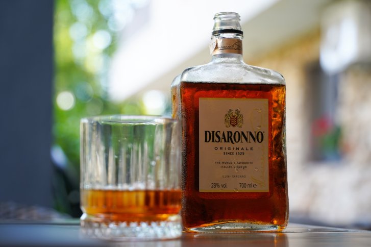 Flasche Disaronno und Glas stehen gefüllt auf einem Tisch im Freien.