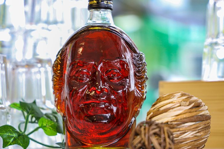 Flasche in Form eines Kopfes steht zwischen Gläsern und Dekorationen auf einem Tisch.