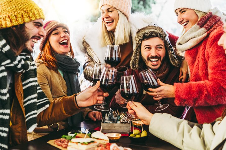 Menschen stoßen mit Rotweingläsern an, während sie draußen warm gekleidet lachen.