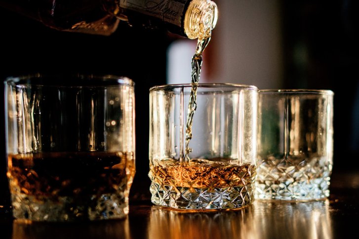 Gläser auf Tisch, ein Glas füllt sich mit goldener Flüssigkeit, warme Beleuchtung.