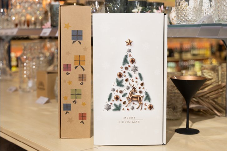 Zwei festliche Geschenkboxen mit Weihnachtsmotiven stehen auf einem Tisch in einem Geschäft.