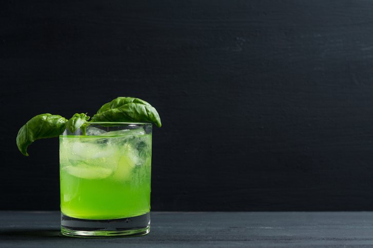 Grünes Getränk mit Eiswürfeln und Basilikum dekoriert, steht auf dunklem, minimalistischen Hintergrund.