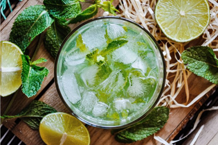 Ein Glas Mojito steht auf Holzbrett, umgeben von Limettenscheiben und Minzblättern.