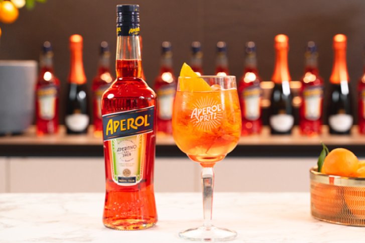 Eine Aperol-Flasche steht neben einem Glas Aperol Spritz auf einem Marmortisch.