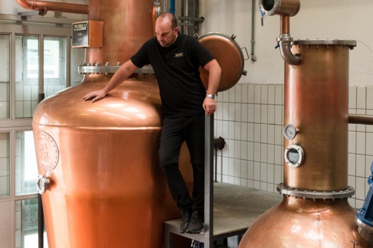 Ein Mann steht auf einer Brennerei-Anlage in einem industriellen Innenraum.